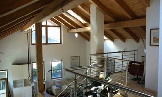A modern, bright living room with high ceilings and wooden beams. Large windows let in plenty of daylight, and a cozy armchair is ready.
