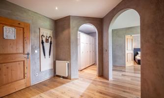 A modern hallway with wooden flooring and gray walls. On the left, umbrellas hang on the wall and a door leads to another room.