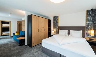 A modern hotel room with a large double bed and a cozy sitting area. The room is bright and cheerfully furnished.