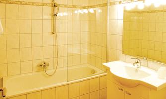 A modern bathroom with a bathtub and sink. Bright tiles and a large mirror surface create an inviting atmosphere.
