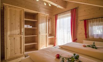 A cozy room with wood paneling and two beds. Large windows with red curtains let in plenty of light.