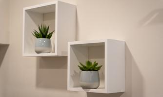 Two modern shelves on the wall with small plants in pots. The shelves are white and give the room a fresh atmosphere.