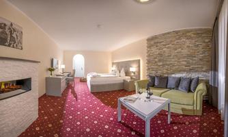 A cozy hotel room with a modern design. There is a double bed, a seating area, and a fireplace that creates a relaxed atmosphere.