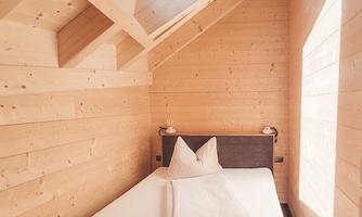 A cozy room with wooden paneling and a large window. The bed is simple and inviting, ideal for a relaxing getaway.