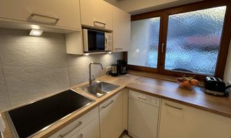 A modern kitchen with bright furniture and a large window front. Fruits and kitchen appliances are on the counter.