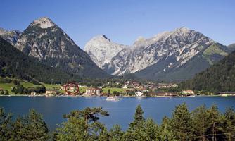 A picturesque mountain landscape with high mountains and a clear blue lake. In the foreground, there are trees and a tranquil environment.