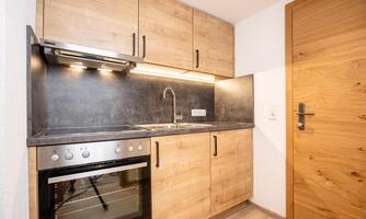 A modern kitchen with wooden cabinets and a black workspace. It features a stove, an oven, and a sink.
