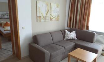 A cozy living room with a gray sofa and a wooden table. Pictures hang on the wall, and the windows have striped curtains.