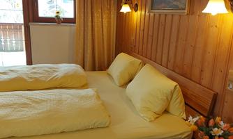 A cozy bedroom with wood paneling and warm light. There are two beds with yellow bedspreads and a small table with flowers.