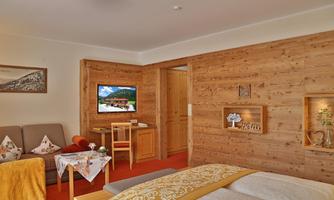 A cozy room with wood paneling and rustic furnishings. There is a double bed, a television, and a seating area with a small table.