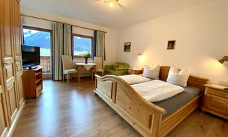 A cozy bedroom with wooden furniture and two beds. The room features a television and a small dining area overlooking the mountains.