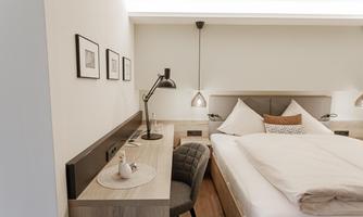 A modern bedroom with a large bed and a desk. The walls are painted in soft tones, and there are decorative pictures.