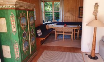 A cozy living space with wooden walls and a green cabinet. The dining area is furnished with a table, chairs, and a lamp.