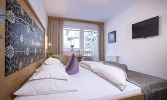 A cozy bedroom with a large bed and bright walls.  
Windows overlooking a snow-covered landscape create an inviting atmosphere.