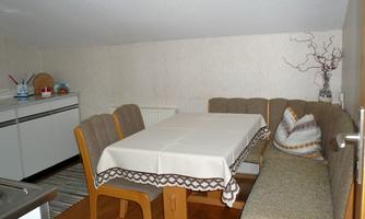 A cozy dining area with a table and upholstered chairs. In the background, there are modern kitchen cabinets and a decorative plant visible.