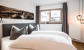 A modern bedroom with two single beds and decorative pillows. Large windows let in a lot of light and create an inviting atmosphere.