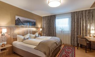 A cozy bedroom with a large bed and soft pillows. The room has a modern style with a desk and beautiful lighting.