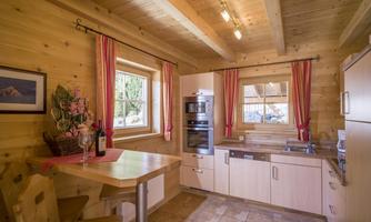 A bright kitchen with wood decor and modern appliances. The windows are adorned with red curtains, and there is a small dining nook.