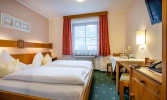 A cozy room with two single beds and a table. Large windows let in plenty of natural light.