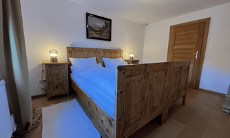 A cozy bedroom with a wooden bed and white bedding. Next to the bed are two lanterns and a large window provides light.