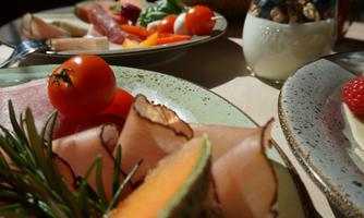 A beautiful breakfast table with fresh fruit, cold cuts, and cheese. In the background, there is a glass with yogurt and granola.