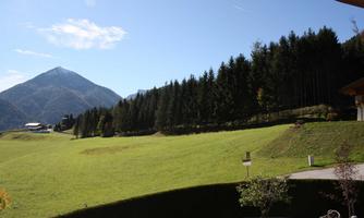 An idyllic landscape with green meadows and a majestic mountain in the background. The sky is clear and blue with a few clouds.