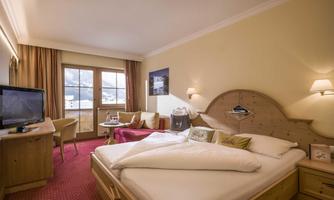 A cozy hotel room with a large bed and a window with a view. The decor is modern and inviting, with warm colors and wooden details.