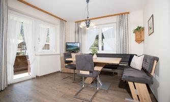 A cozy living area with a dining table and a bench. Large windows let in plenty of light, and the decor is modern and inviting.