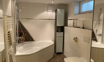 A modern bathroom with a bathtub and a shower. The walls are light tiled and the room is well lit.