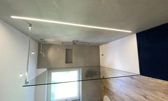 A modern shower with glass partition and LED lighting. The bathroom area is bright and inviting, with wooden flooring and a window.