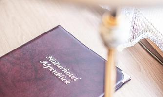 An elegant clipboard lies on a table next to a table lamp. The clipboard bears the inscription "Naturhotel Alpensicht".