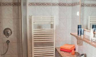 A modern bathroom with a shower, a sink, and a towel rack. The walls are tiled and there are some toiletries on the shelf.