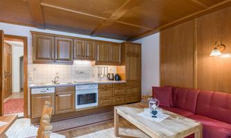 A cozy apartment with a wooden kitchen and a red sofa. The room has warm lighting and plenty of space to relax.