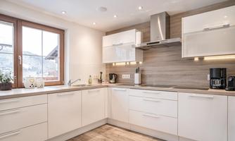 A modern kitchen with white furniture and wood paneling. There are windows that let in a lot of daylight.