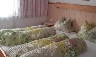 A cozy bedroom with a large double bed. The bedding is colorful patterned, and the room has bright curtains and a friendly atmosphere.