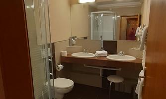 A modern bathroom with a shower, two sinks, and elegant lighting. The walls are in neutral colors and the floor is covered with dark tiles.