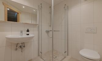 A modern bathroom with a shower cabin and a sink. The walls are light tiled and there is a window for daylight.