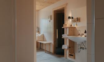 A modern bathroom with wood-paneled walls. There is a washbasin and a cozy seating area.
