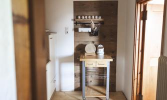 A cozy entrance area with a wooden shelf and a small table. The room has a warm, inviting atmosphere.