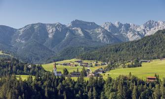 A picturesque mountain landscape with a small village and a church in the foreground. The majestic mountains rise in the background, surrounded by green meadows and forests.