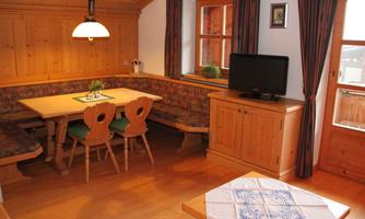 A cozy dining area with wooden furniture and a bench. A television and a window create a bright atmosphere.
