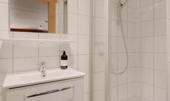 A modern bathroom with a shower cabin and a sink. The walls are covered with white tiles and the ceiling is made of wood.