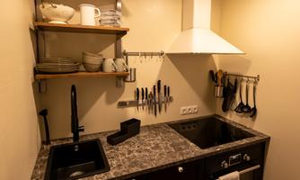 A modern kitchen unit with a black countertop and a sink. Shelves above are decorated with dishes and cooking utensils.