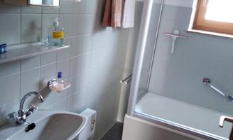 A small bathroom with a bathtub and a shower cabin. The walls are lightly tiled, and there is a mirror above the sink.