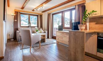 A cozy living room with large windows and a view of the mountains. The decor is modern and inviting, with a sofa and a small kitchenette.