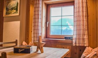 A cozy room with a wooden table and chairs. Through the window, one can see the mountain landscape.