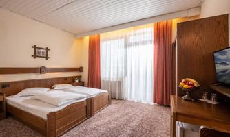 A cozy hotel room with two beds and large windows. The decor is simple, with a TV and a table on which fresh fruit is placed.