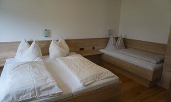A cozy bedroom with two single beds and an additional sleeping space. The walls and furniture are made of light wood, creating a warm atmosphere.