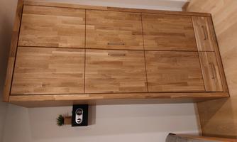 A modern wooden cabinet with two doors and drawers stands in a quiet room. Next to the cabinet is a small plant and a wall shelf with a clock.