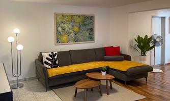 A modern living room with a gray couch and colorful cushions. There is also a small coffee table, a floor lamp, and plants.